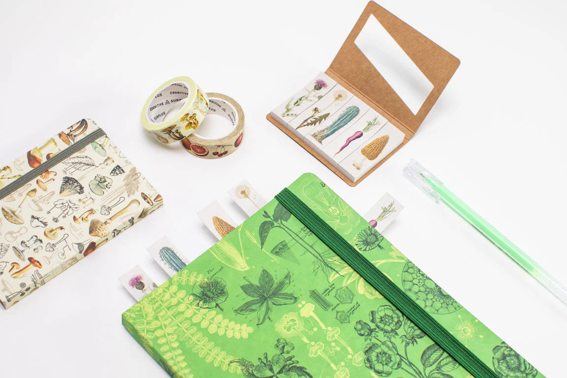 An assortment of stationery items including a green notebook with plant designs, two rolls of decorative tape, a small folder with botanical stickers, and a translucent green pen.